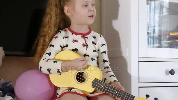 Criança brincando ukulele no sofá — Vídeo de Stock