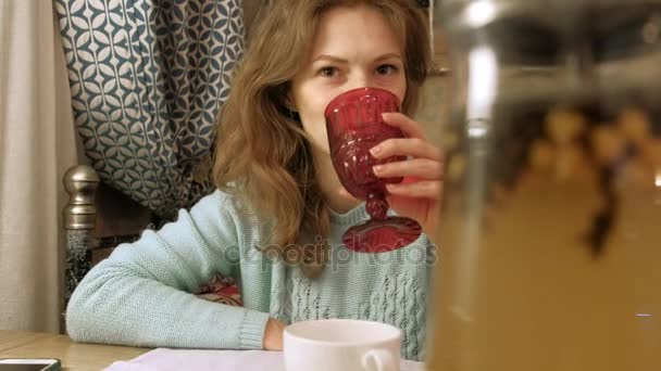 Щаслива дівчина п'є чай і розслабляється в кафе, посміхаючись і дивлячись на камеру . — стокове відео