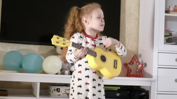 Niño pequeño jugando ukelele en el sofá — Vídeo de stock