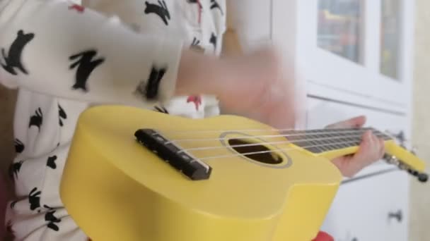 Маленький ребенок играет на укулеле на диване — стоковое видео