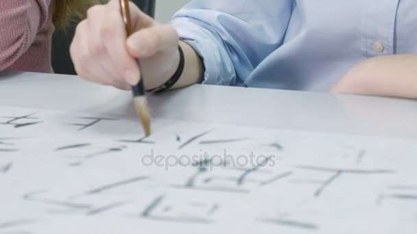 Mujer enseñando a los adolescentes a escribir caracteres chinos en la clase de caligrafía. Estudiante aprendiendo a escribir con pincel, tinta, papel y profesor ayudándola. Escuela, educación — Vídeo de stock