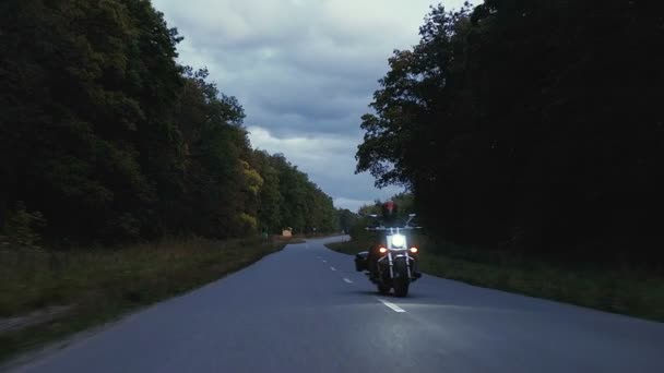 En man rider motorcykel ner en väg i skogen — Stockvideo