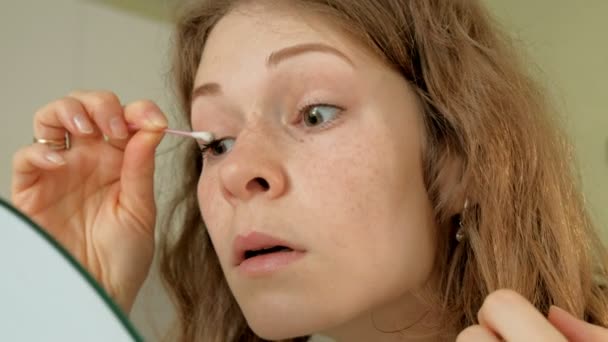 Ung kvinna att sätta på mascaran och titta i hand spegel i sovrummet hemma — Stockvideo