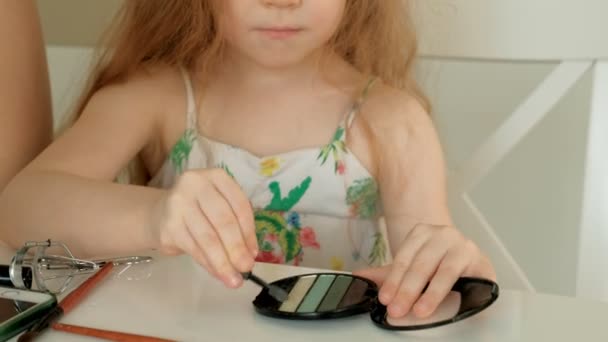 Маленька дівчинка дивиться, як її мати готується вдома і грає зі своїм макіяжем . — стокове відео