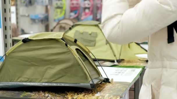 Jonge vrouw in een speciaalzaak voor het toerisme pakt camping tent — Stockvideo