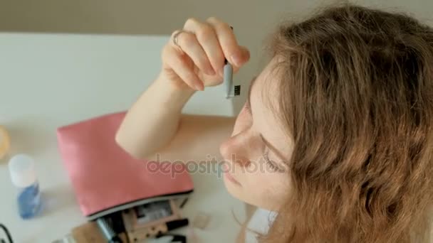 Молодая женщина надевает тушь и смотрит в ручное зеркало в спальне дома — стоковое видео