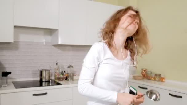Счастливая кудрявая девушка танцует на кухне дико волосы прыгая платье дома с диким весельем слушать музыку — стоковое видео