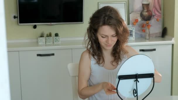 Young woman putting on mascara and looking in hand mirror in bedroom at home — Stock Video