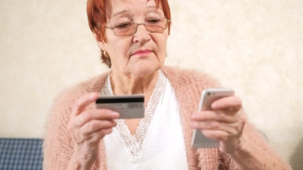 Yaşlı bir kadın alışveriş yapar için kredi kartı ve telefon aktarmak bir banka öder — Stok video