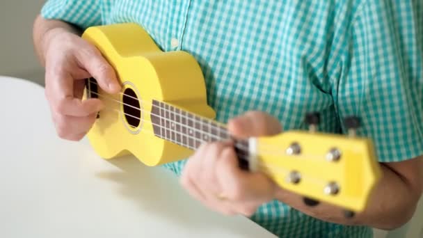 Un hombre juega con un ukelele de color amarillo — Vídeo de stock
