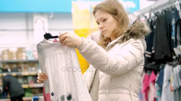 En ung kvinna i en stormarknad köper kläder — Stockvideo