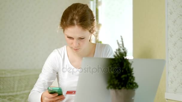 Una mujer joven compra bienes en una tienda en línea y paga una tarjeta de crédito a través de su teléfono — Vídeos de Stock