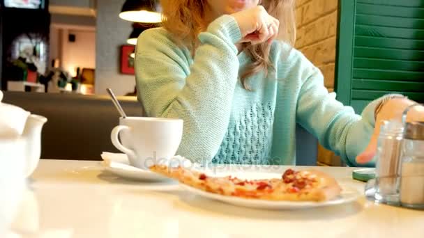 Mooie jongedame in een restaurant eten van pizza en drinken thee — Stockvideo