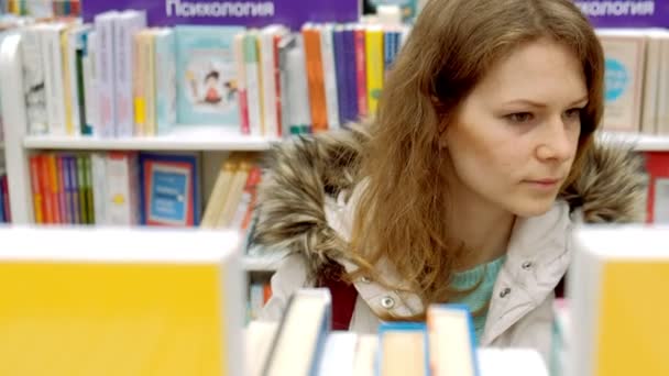 Mulher lendo um livro que ela acabou de remover para uma exibição em uma prateleira em uma livraria — Vídeo de Stock