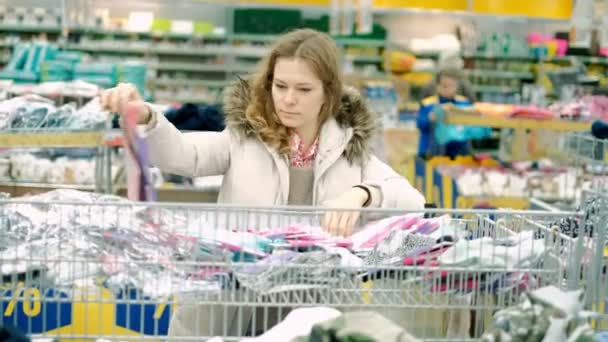 Μια νεαρή γυναίκα σε ένα σούπερ μάρκετ αγοράζει ρούχα — Αρχείο Βίντεο