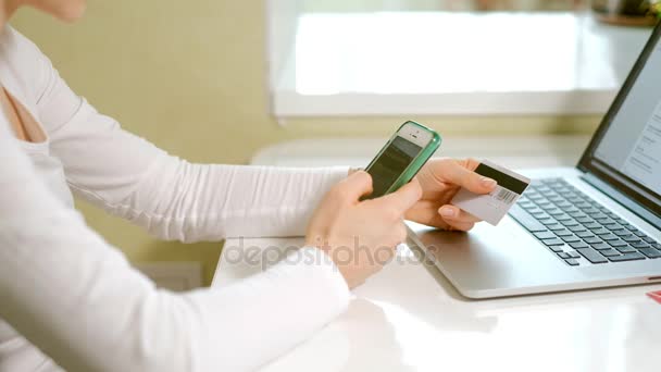 En ung kvinna köper varor i en onlinebutik och betalar ett kreditkort via sin telefon — Stockvideo