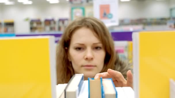 Woman reading a book which she has just removed for a display on a shelf in a bookstore — Stock Video