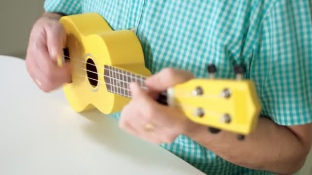 Een man speelt op een ukulele van gele kleur — Stockvideo