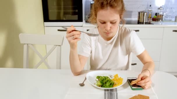 Uma bela mulher come brócolis e ervilhas verdes com prazer, à mesa em casa — Vídeo de Stock