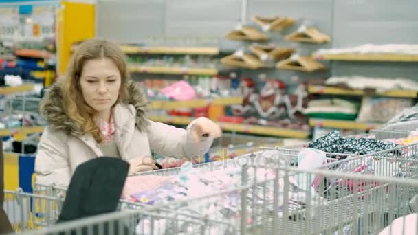 Eine junge Frau im Supermarkt kauft Kleidung — Stockvideo