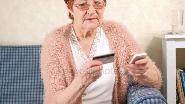 An old woman pays for purchases makes a bank transfer by credit card and phone — Stock Video