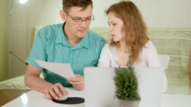 Усміхнена молода пара, використовуючи ноутбук вдома емоційно обговорює — стокове відео