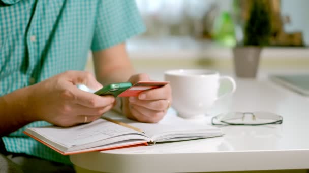 Een man koopt goederen in een online winkel, en betaalt een creditcard via haar telefoon — Stockvideo