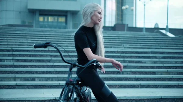 Mulher bonita monta uma bicicleta perto de um prédio alto — Fotografia de Stock