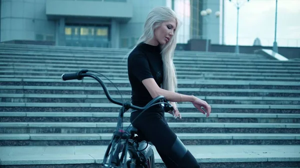 Mulher bonita monta uma bicicleta perto de um prédio alto — Fotografia de Stock