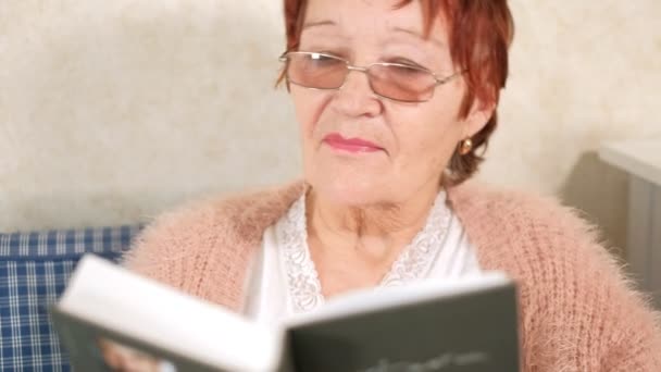 Vieja leyendo un libro en el sofá de casa — Vídeo de stock