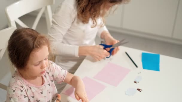 Eine Frau mit einem Mädchen bei einer Applikation von buntem Papier, die zu Hause an einem Tisch sitzt — Stockvideo