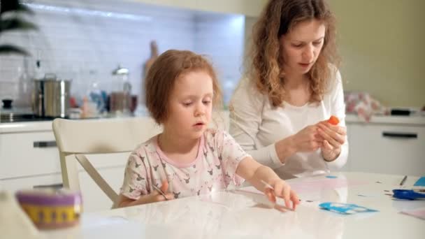 A woman with a girl doing an application of colored paper sitting at a table at home — Stock Video