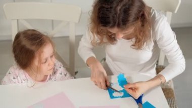 Bir kadın bir kızla renkli kağıttan bir masada evde oturan bir uygulama yapıyor
