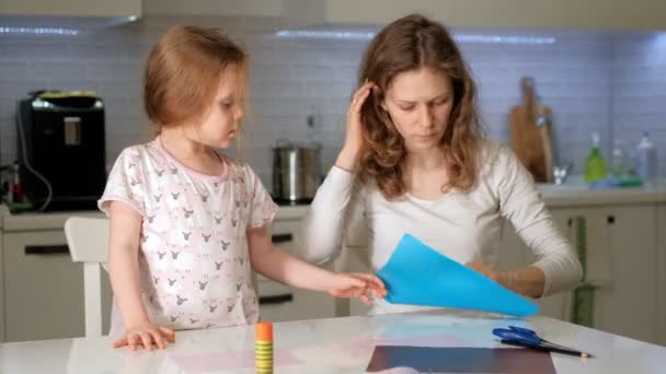 En kvinna med en tjej som gör en ansökan av färgat papper sitter vid ett bord hemma — Stockvideo