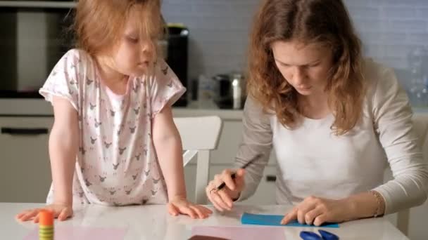 Женщина с девушкой, которая делает заявление из цветной бумаги, сидя за столом дома — стоковое видео