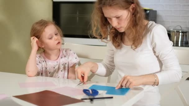 Een vrouw met een meisje doen van een aanvraag van gekleurd papier zitten aan een tafel thuis — Stockvideo