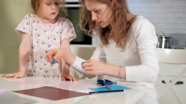 Una mujer con una chica haciendo una aplicación de papel de color sentada en una mesa en casa — Vídeo de stock