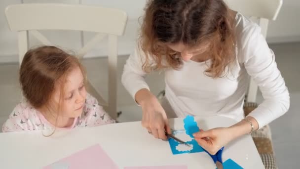 Uma mulher com uma menina fazendo uma aplicação de papel colorido sentado em uma mesa em casa — Vídeo de Stock