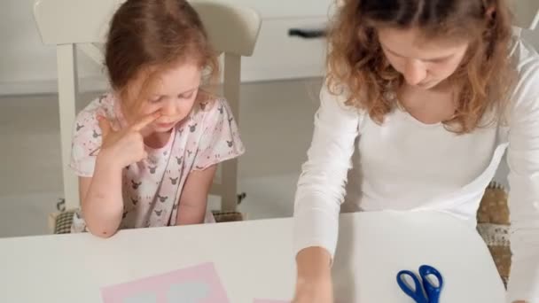 Uma mulher com uma menina fazendo uma aplicação de papel colorido sentado em uma mesa em casa — Vídeo de Stock