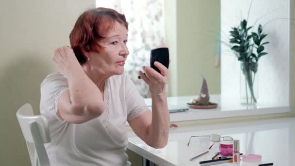 Gammal kvinna gör en makeup framför en spegel hemma — Stockvideo