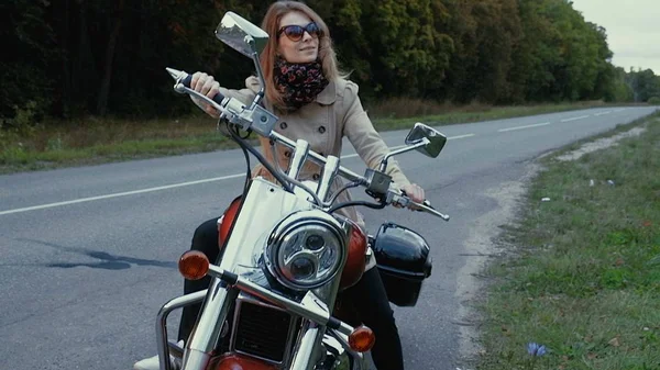 Jovem com cabelo castanho senta-se em uma moto perto de uma estrada . — Fotografia de Stock