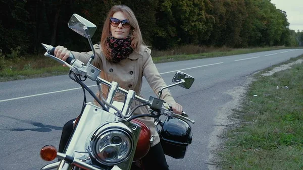 Nuori tyttö ruskeat hiukset istuu moottoripyörä lähellä tietä . — kuvapankkivalokuva