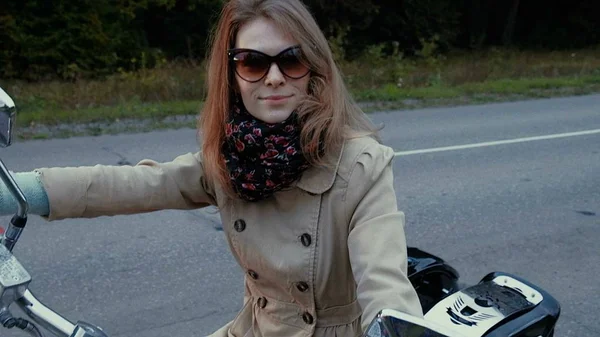 Молода дівчина з коричневим волоссям сидить на мотоциклі біля дороги . — стокове фото