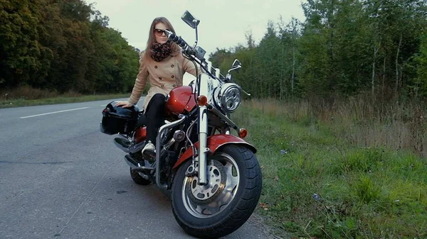 Молодая девушка с каштановыми волосами сидит на мотоцикле возле дороги . — стоковое фото