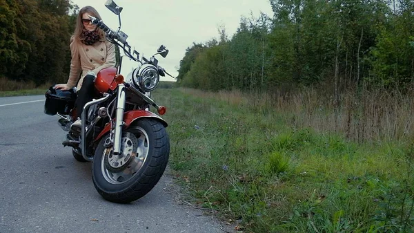 Chica joven con el pelo castaño se sienta en una moto cerca de una carretera . — Foto de Stock