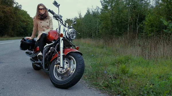 Junges Mädchen mit braunen Haaren sitzt auf einem Motorrad in der Nähe einer Straße. — Stockfoto