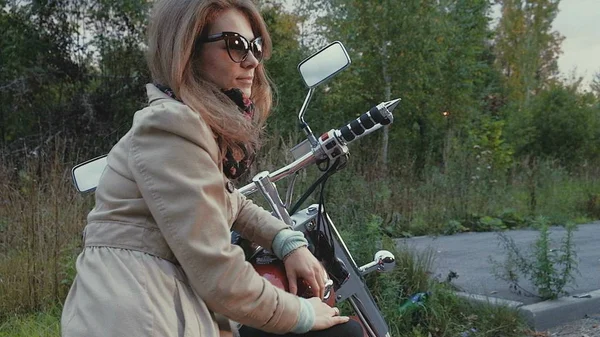 Jeune fille aux cheveux bruns s'assoit sur une moto près d'une route . — Photo