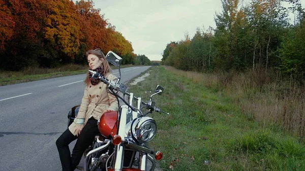 Młoda dziewczyna o brązowych włosach siedzi na motocyklu w pobliżu drogi. — Zdjęcie stockowe