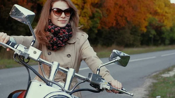 Chica joven con el pelo castaño se sienta en una moto cerca de una carretera . —  Fotos de Stock