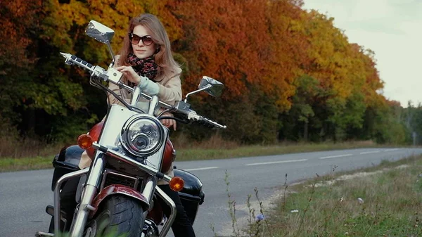 Chica joven con el pelo castaño se sienta en una moto cerca de una carretera . — Foto de Stock